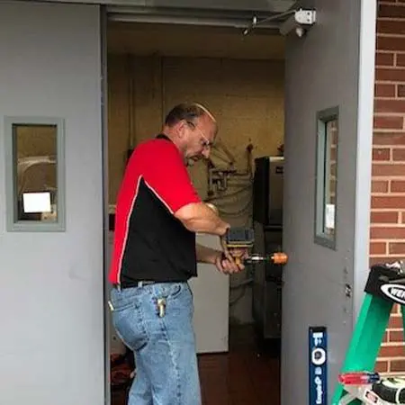 Door security specialist drills hole for electronic exit device installation near Leominster, MA